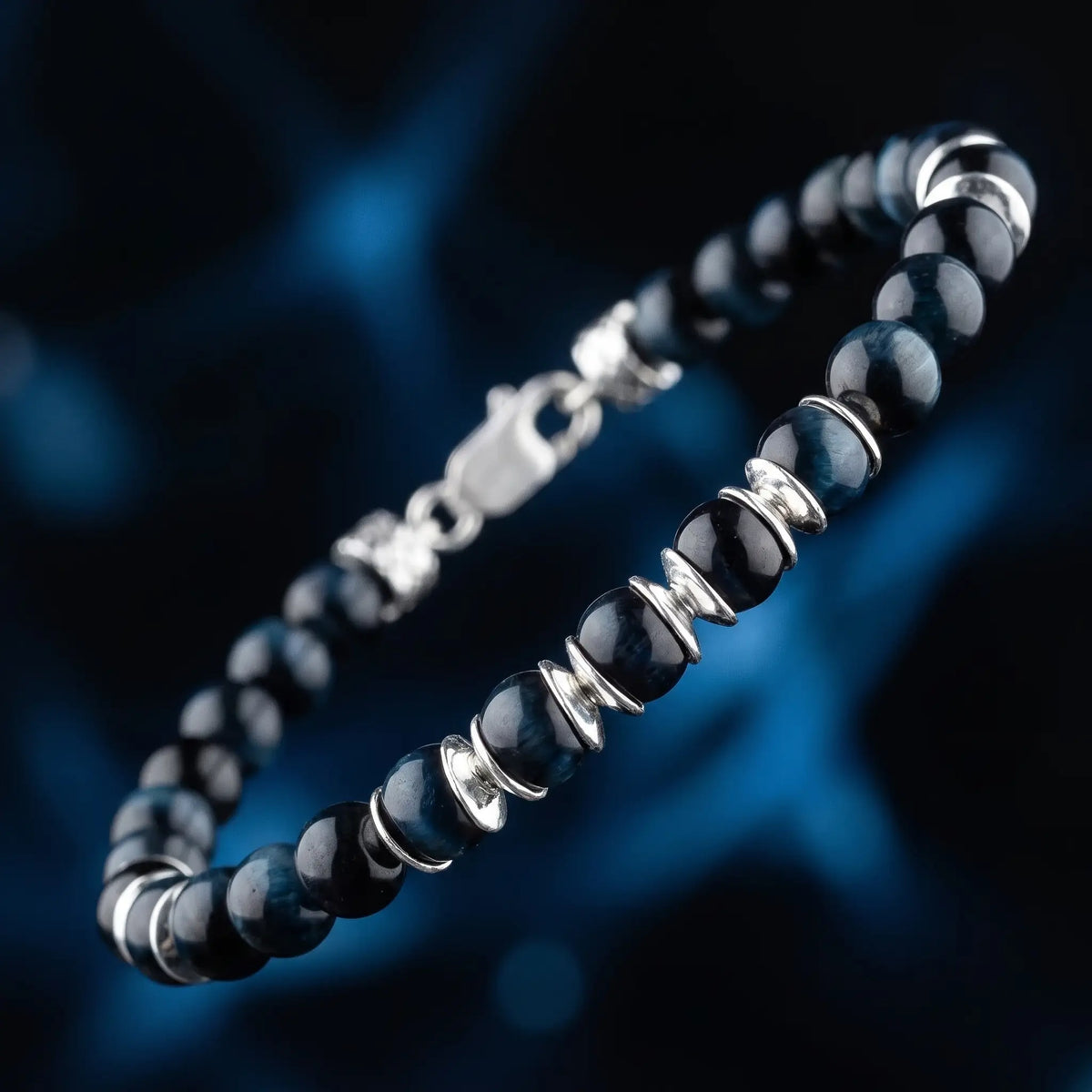 Blue Tiger Eye Bracelet IV (6.5mm) by Aurum Brothers, angled view with sculpted silver spacers against a dark blue background.