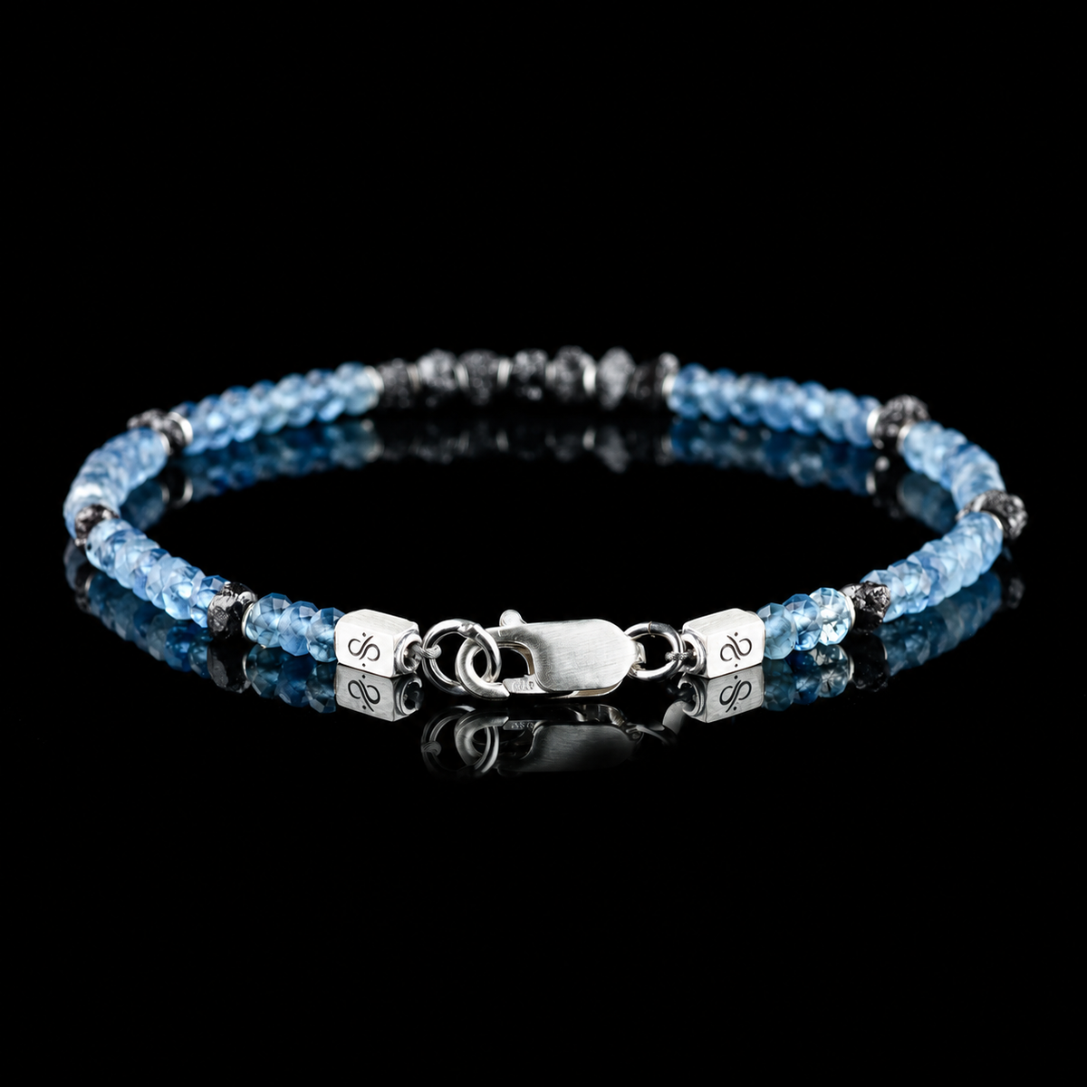 Back view of Raw Black Diamond - Aquamarine Bracelet I (4mm), showing the clasp and branded end pieces on a black reflective surface.